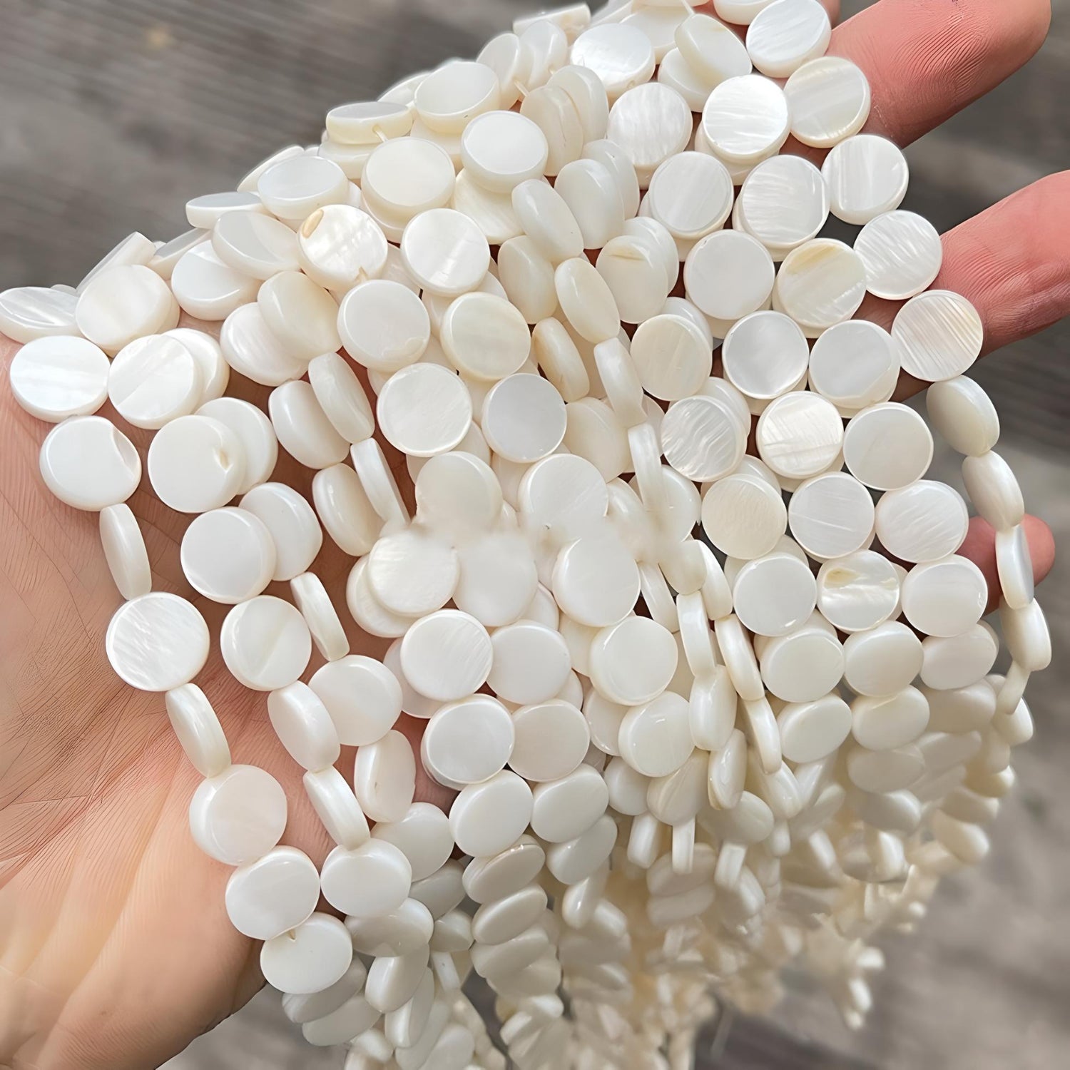 someone holding strings of flat freshwater shell beads in ivory color