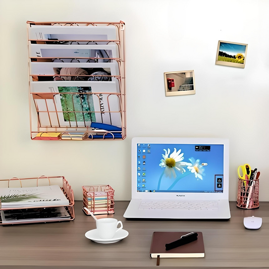 A desktop with a computer and a rose gold wall file organizer.