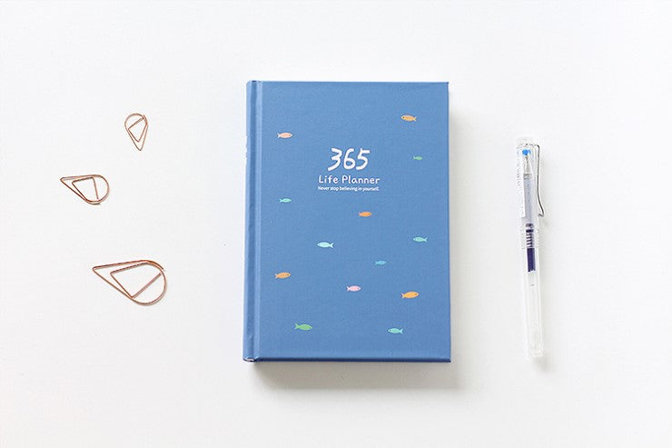 planner on a desk with a gel pen and paper clips beside