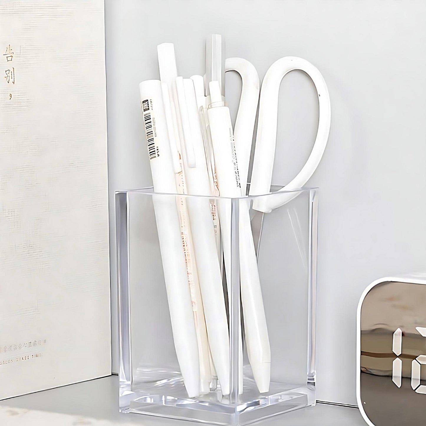 a bunch of white gel pens and a pair of scissors in a transparent pen holder, on a grey desk